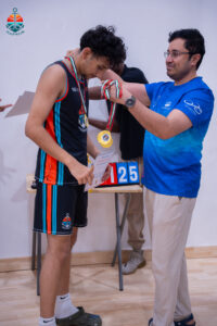 Harbor Sports Academy coach handing a medal to a player at the tournament awards table